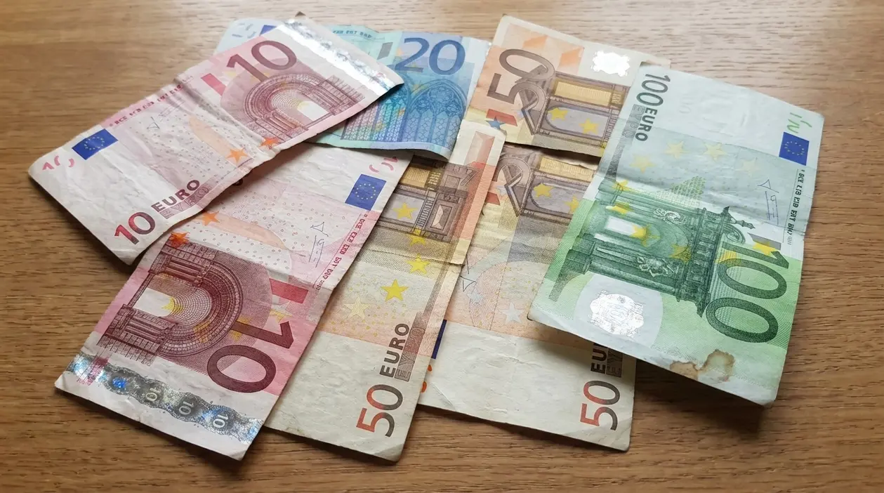 Banconote in euro usurate e piegate appoggiate su un tavolo, tra cui 10, 20, 50 e 100 euro