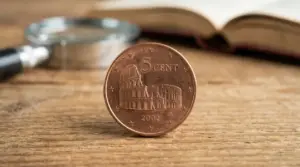 Moneta italiana da 5 centesimi con il Colosseo in primo piano su un tavolo, con lente e libro sullo sfondo