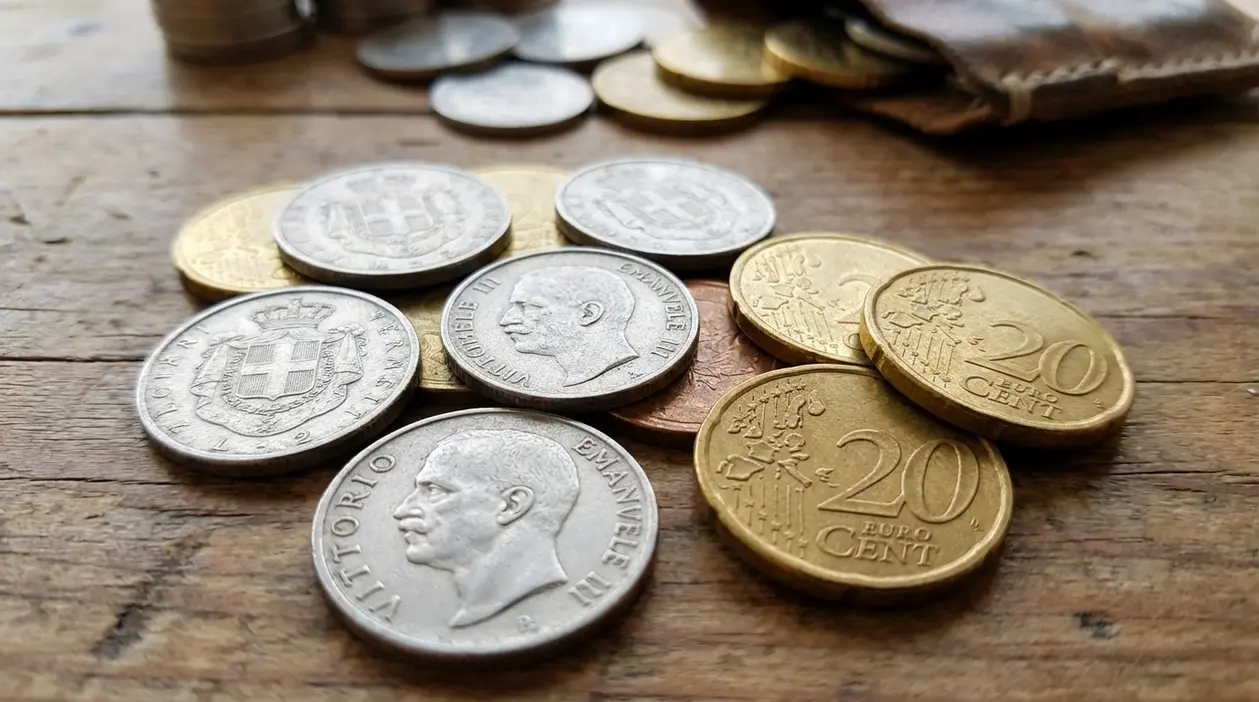 Monete da 20 centesimi e vecchie lire italiane sparse su un tavolo di legno