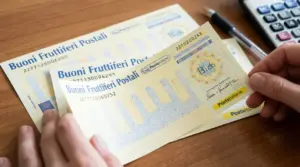 Persona che tiene in mano alcuni buoni fruttiferi postali su un tavolo con penna e calcolatrice