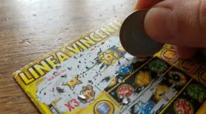 Mano che gratta un biglietto Gratta e Vinci con una moneta, cercando un simbolo nascosto vincente