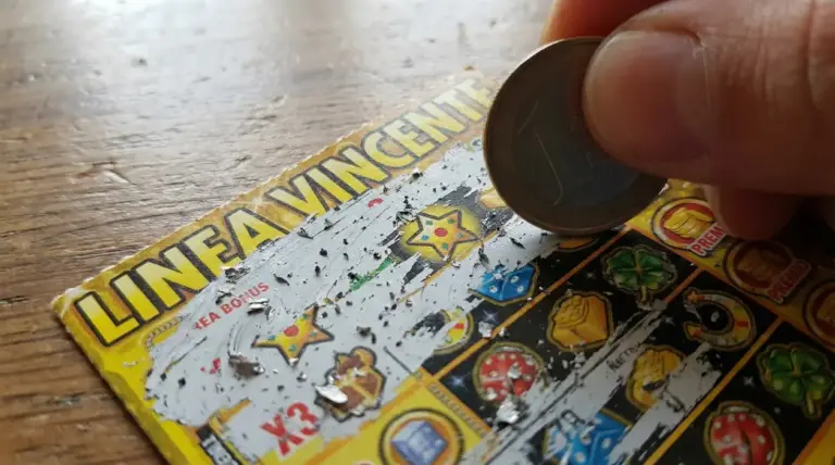 Mano che gratta un biglietto Gratta e Vinci con una moneta, cercando un simbolo nascosto vincente