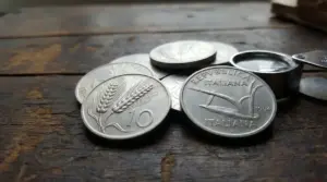 Monete da 10 lire con la spiga su un tavolo di legno, accanto a una lente per il controllo numismatico