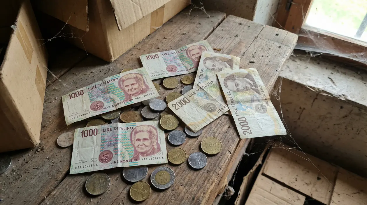 Vecchie lire italiane, banconote e monete, ritrovate su un tavolo impolverato in soffitta
