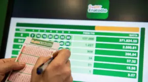 Persona che compila una schedina del Superenalotto davanti a uno schermo con risultati e quote della vincita
